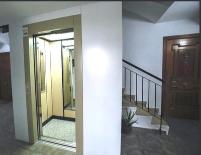 Ascensor abierto junto a escaleras de subida a plantas superiores de un edificio residencial
