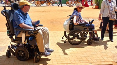 Dos ciudadanos se desplazan en silla de ruedas por la feria de Sevilla