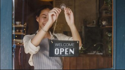 Una mujer cuelga un cartel en la puerta de entrada de un negocio indicando que está abierto